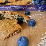 Wood cutting board with blueberry oatmeal cooking cut in half. Fresh blueberries around and plate of cookies in background