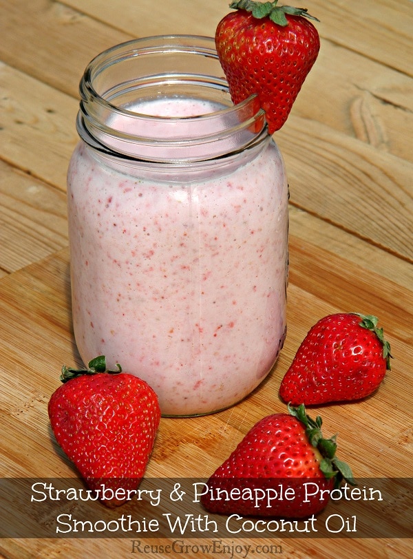 Mason jar filled with strawberry and pineapple protein smoothie with fresh strawberry on side of mouth of jar and some laying beside the jar