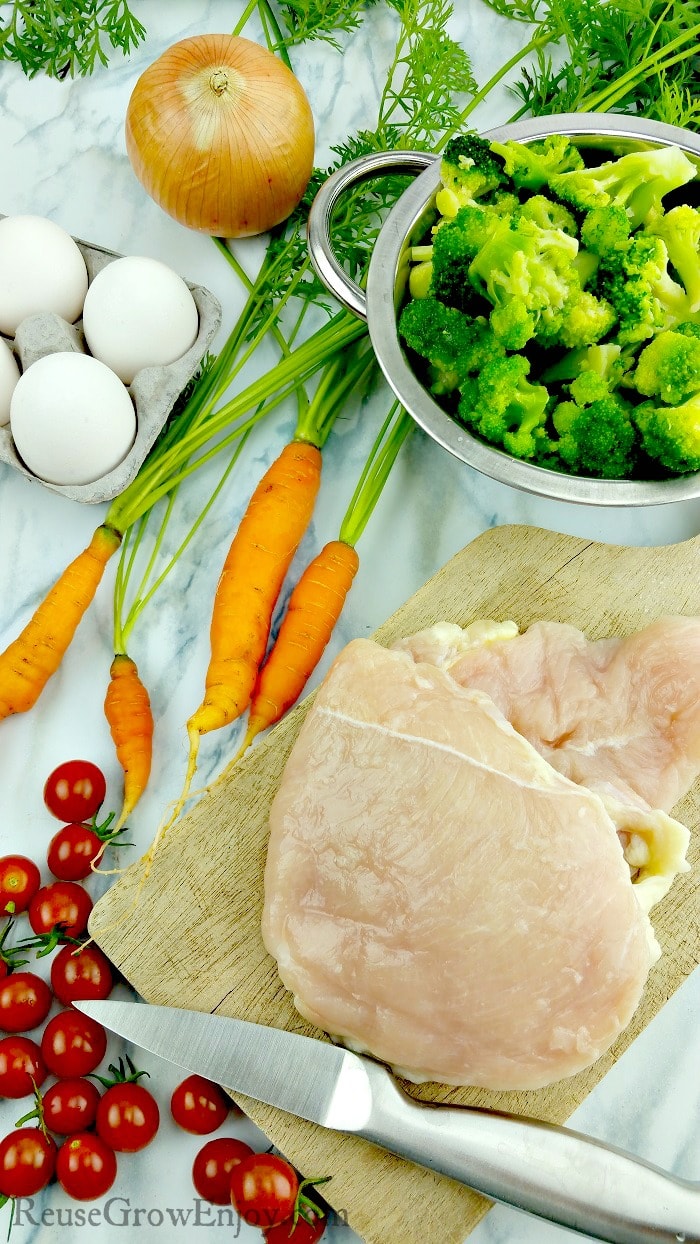 fresh produce of carrots, cherry tomatoes, onions and broccoli with white fresh eggs on the side and raw chicken breast on a wood cutting board for learning Keto hacks.