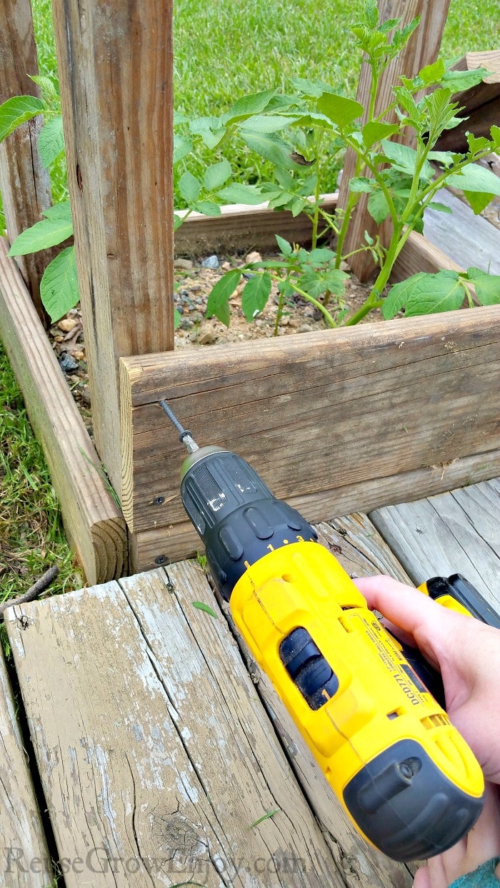 Hand holding a drill adding the 2nd round of boards to the tower.