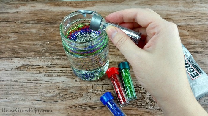 Hand adding different colors glitters to jar filled with oil.