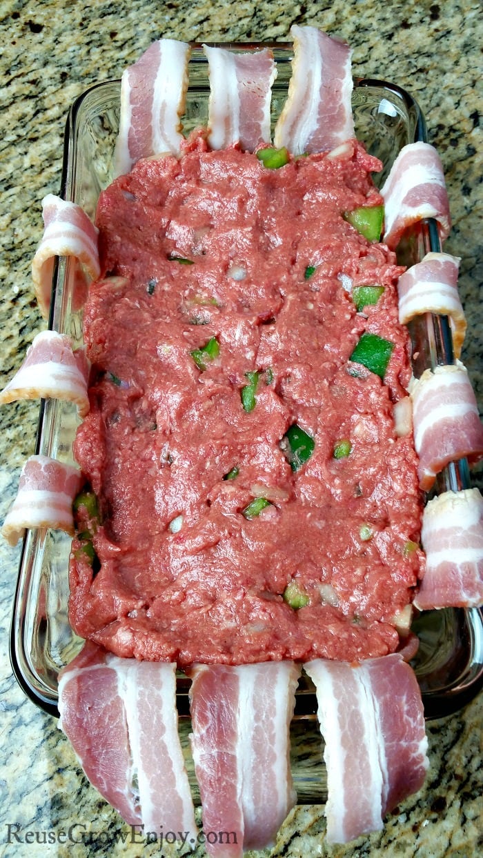 Meatloaf mixture in the center of the bacon lined glass loaf pan.