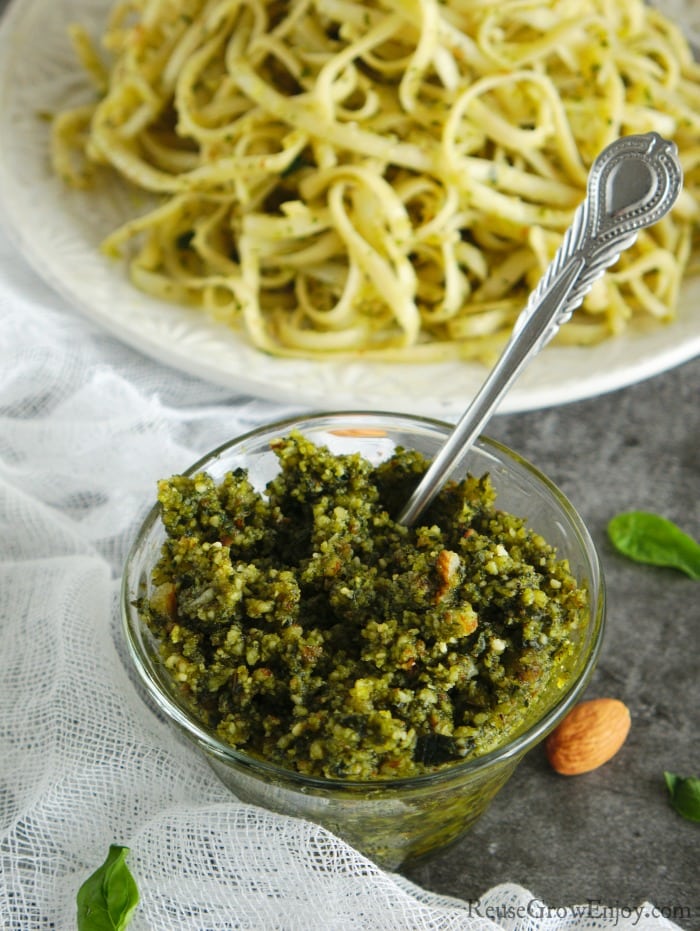 Small glass bowl of homemade pesto with plate of pasta in background.