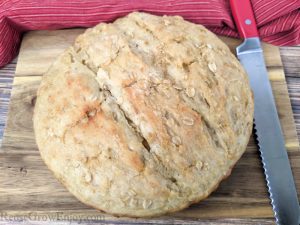 Fresh baked round loaf of honey oat bread on cutting board with knife to side