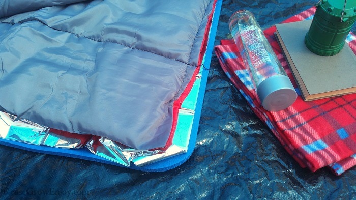Emergency Blanket between sleeping bag and sleep pad. Blanket, bottle of water, camping light and book to the right.