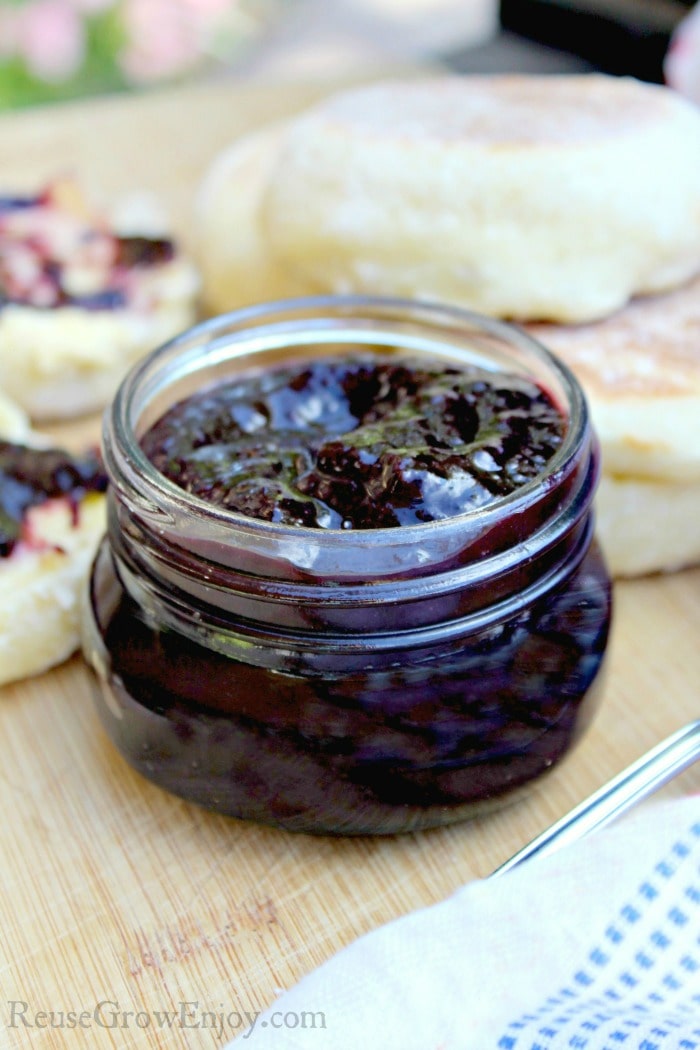 Glass jar full of blueberry butter and English muffins in the background.