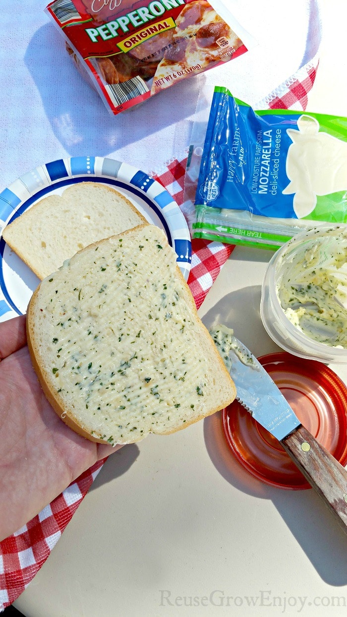 Slice or bread being buttered with garlic butter.