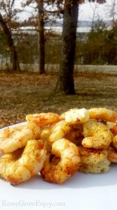 Campfire shrimp on white plate with woods and lake in background.