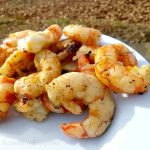 Cooked campfire shrimp on white plate with leaves in background.