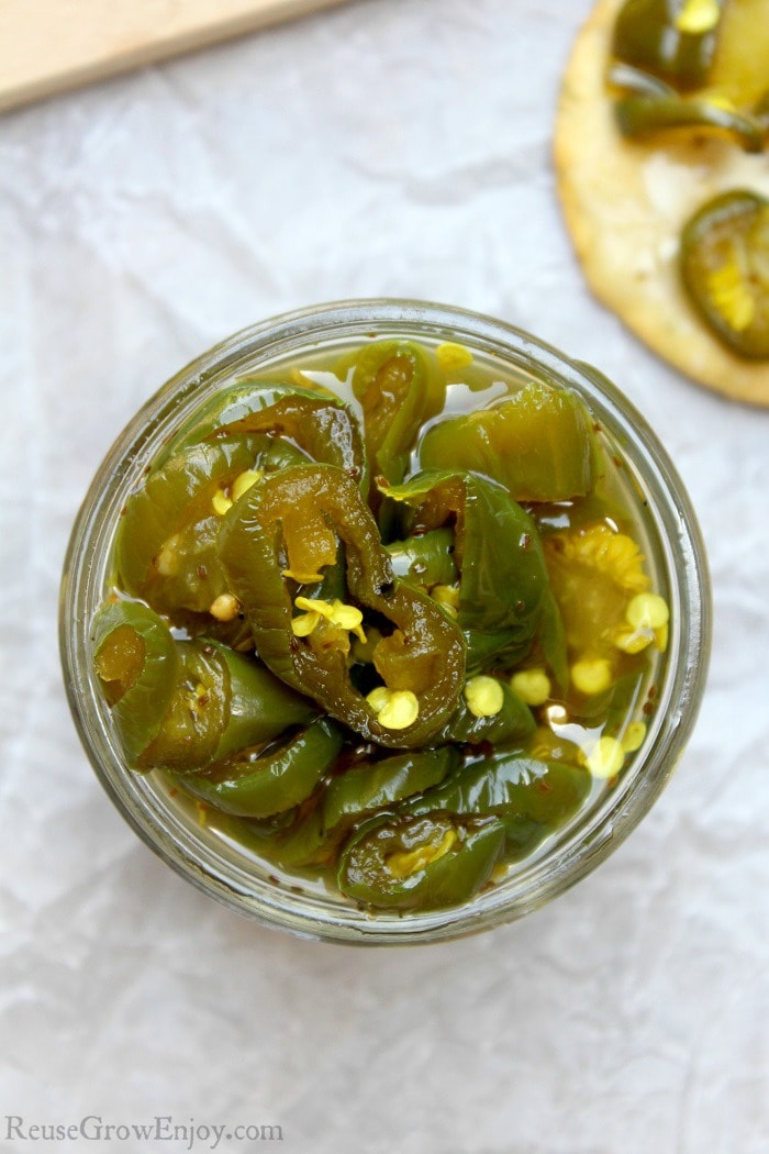 Overhead view of glass jar full of cowboy candy with lid off. Cracker with cream cheese and peppers on it to the side.