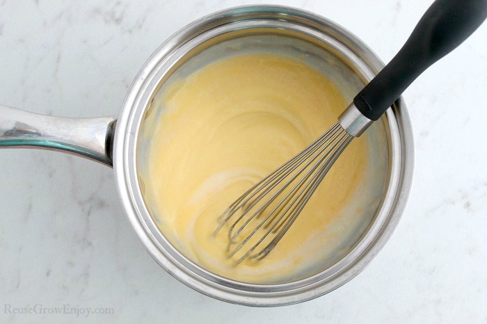 Small pot with hot milk and cheese being whisked together.