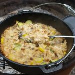 Chicken And Squash Dutch Oven Casserole sitting by side of campfire