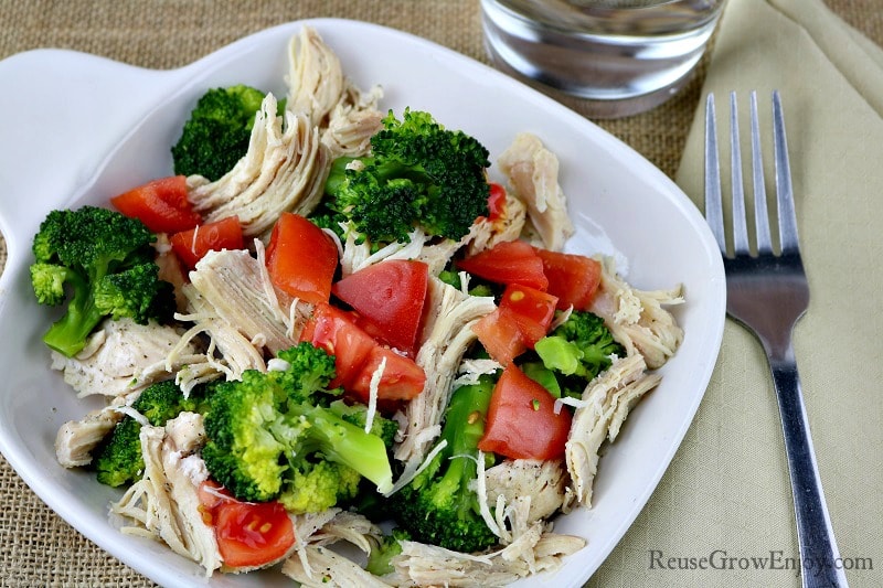 White plate with tomatoes, broccoli and lemon pepper chicken fork at right side of plate.