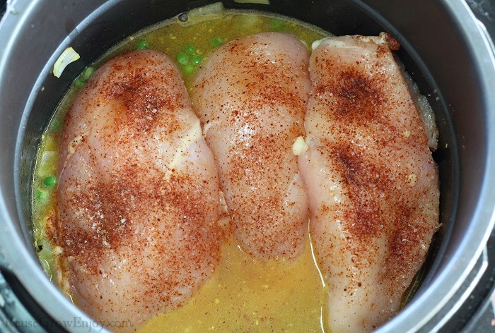 Season coated chicken breasts in broth in a pot.