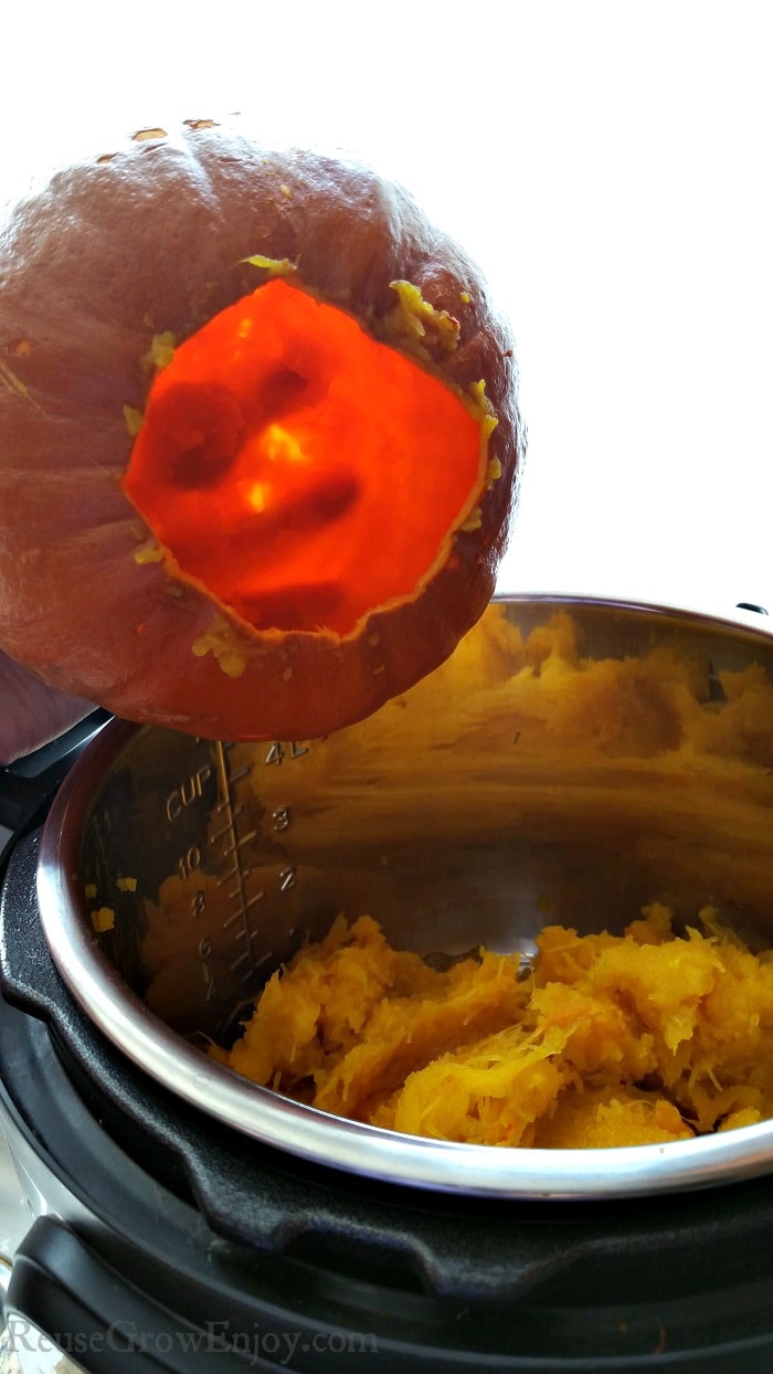 Hand holding a scooped out pumpkin shell with the pumpkin puree inside the Instant Pot.