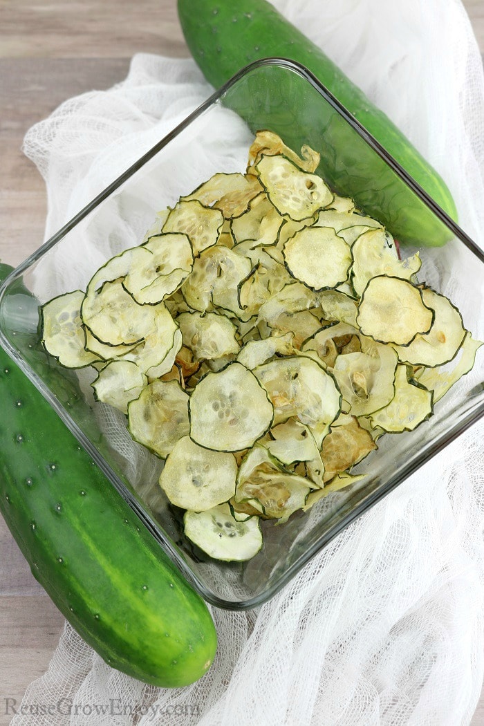 Bowl of cucumber chips with raw cumbers on each side.