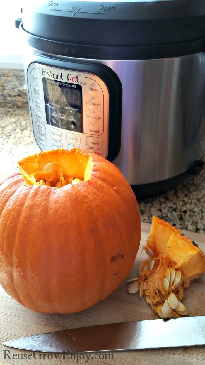Small whole pumpkin with the top center cut out and laying beside it on a cutting board with a knife.