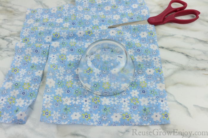 Scissors cutting fabric with glass bowl on fabric