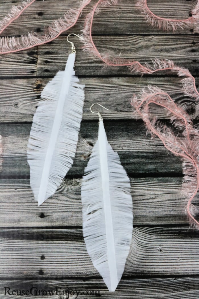 White ribbon feather earrings on wood background