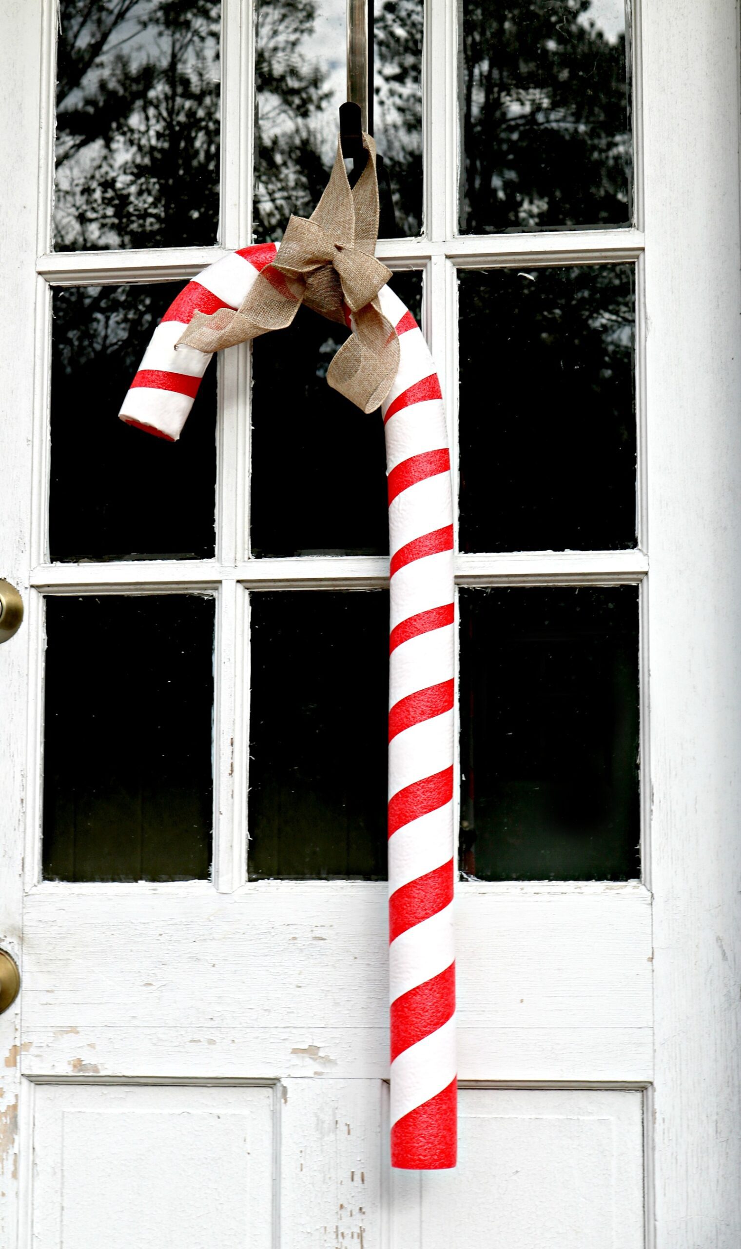 Large red and white striped candy cane hanging on a door with a burlap bow.