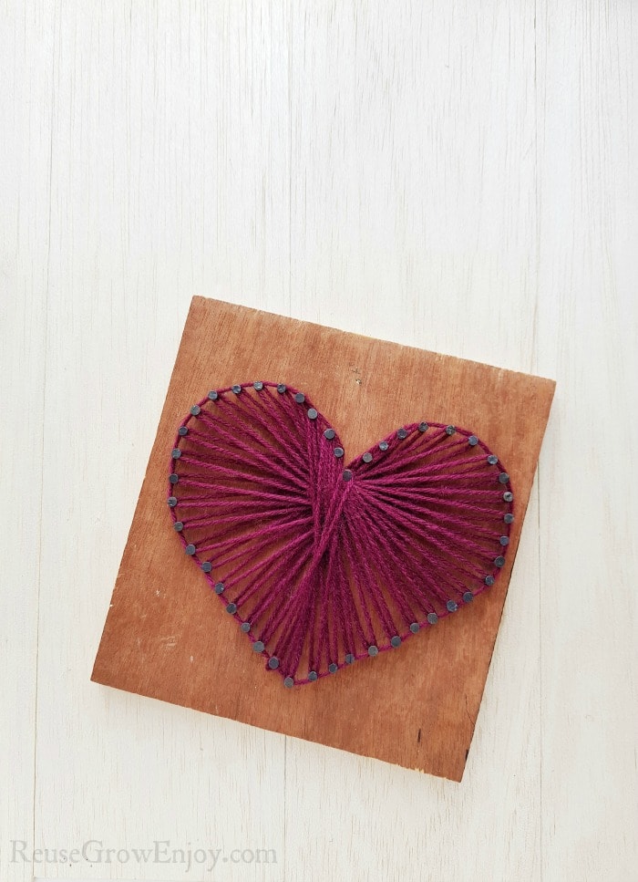 Heart string art on wood board with purple string.