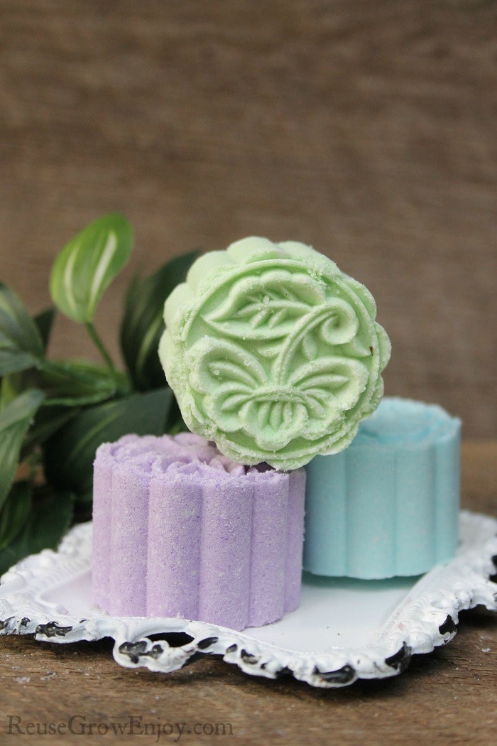 Three pressed bath bombs on a white tray with leaves in the background.