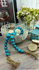 DIY paper mache bowl with farmstyle beads in it and picture and flowers in the background.