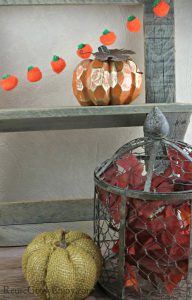 Pumpkin garland hanging on barn wood shelf with fall decor in the front.