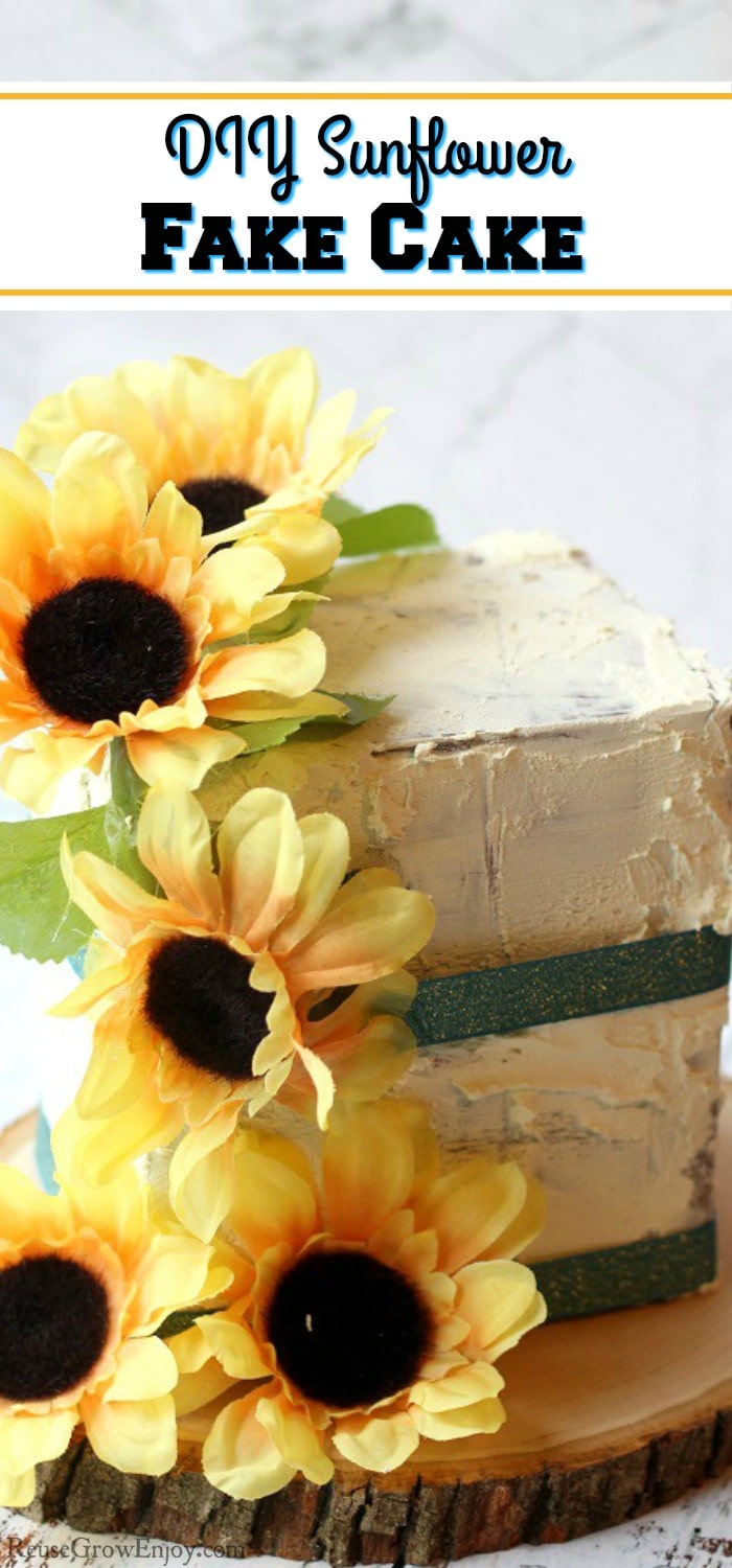 A finished fake cake prop with sunflowers and green ribbon. It is on a wood slice. Text overlay that says "DIY Sunflower Fake Cake".