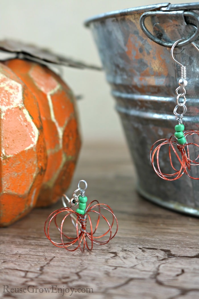 Pair of wire pumpkin earrings with a fake pumpkin and tin in the background.