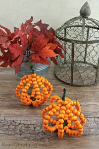 Wood bead pumpkins with read leaves and wire decor in background.