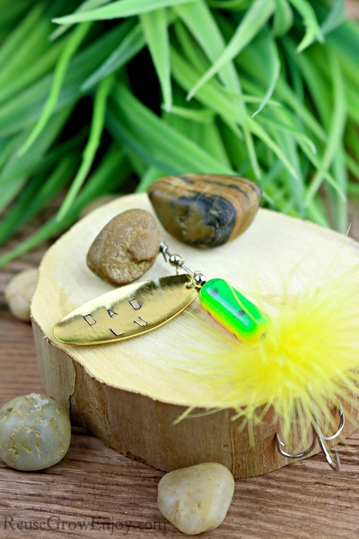 Dad Fishing Gift Idea- Hand stamped fishing lure laying on wood with rocks.