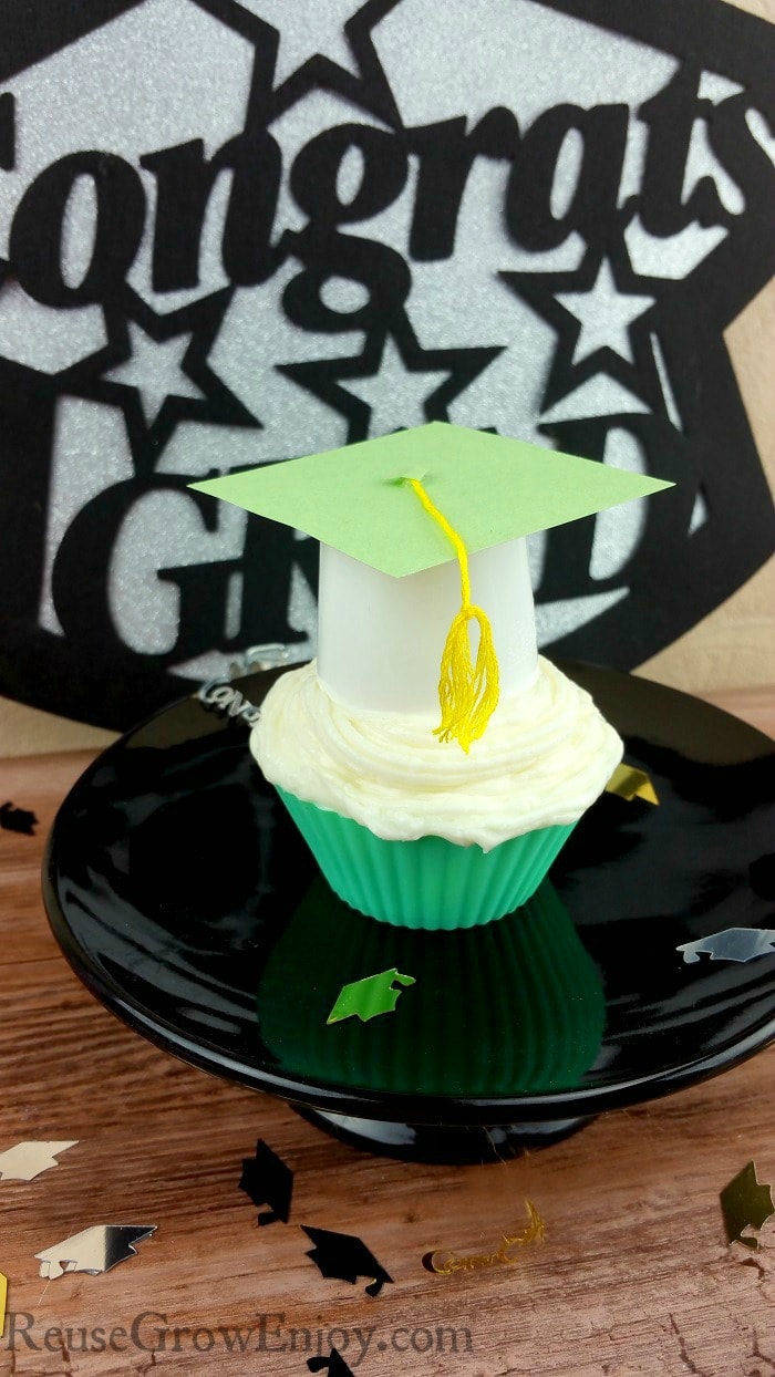 Graduation cupcake toppers on a cupcake on a black cake stand.