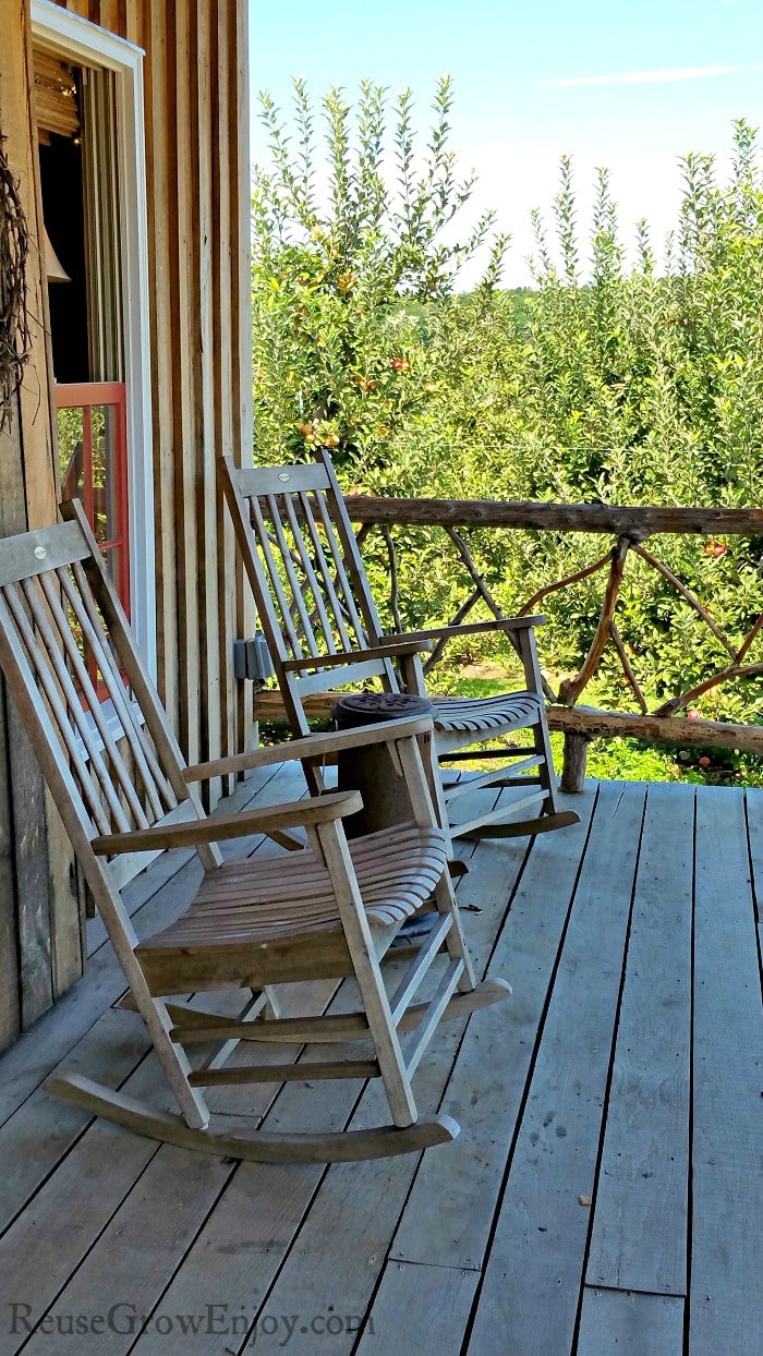 Old style porch with two wood rocking chairs, apple trees in the background. 