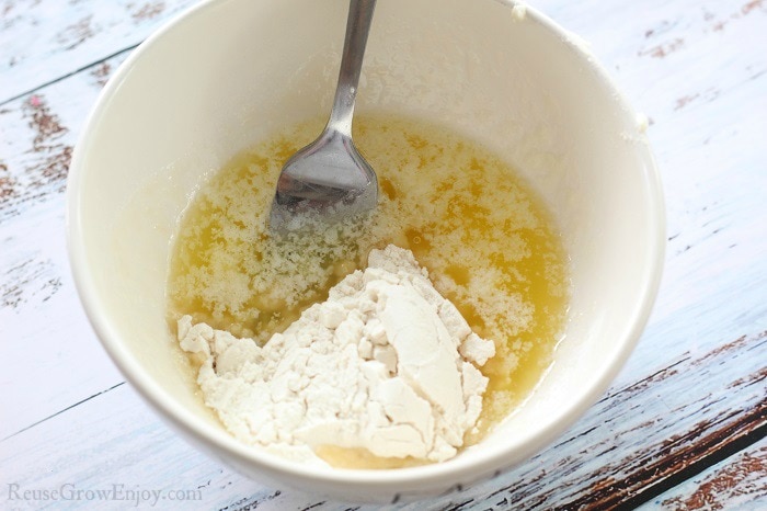 White mixing bowl with melted butter, egg and flour being mixed with a fork.