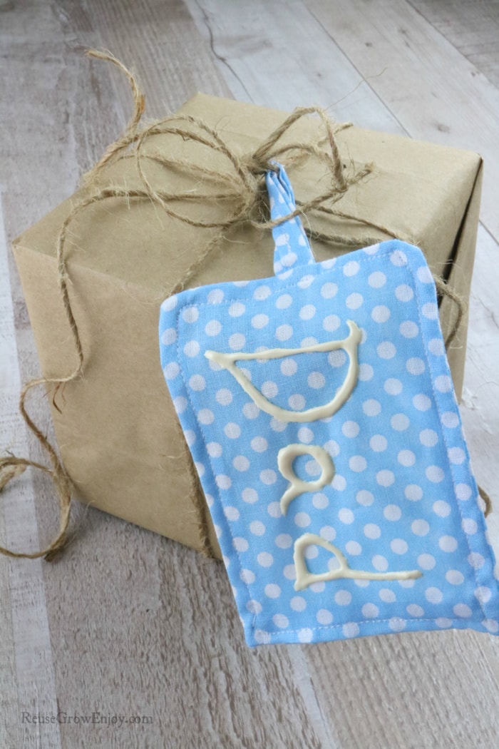 Small box wrapped in brown paper with twine bow and blue and white dotted fabric gift tag hanging off