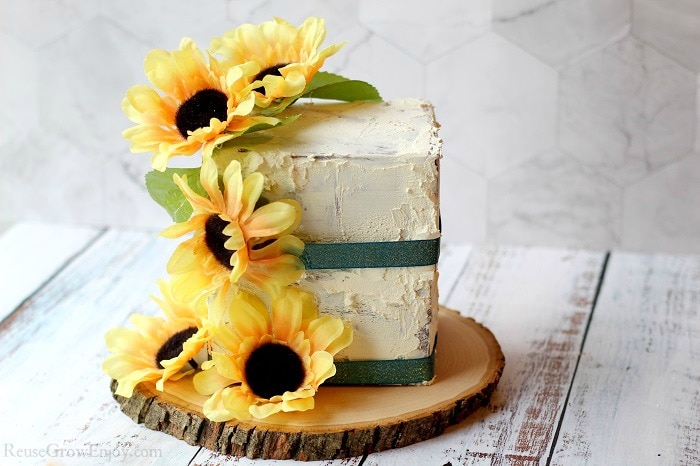 Finished fake cake prop with sunflowers on a wood slice. Laying on white wood background.