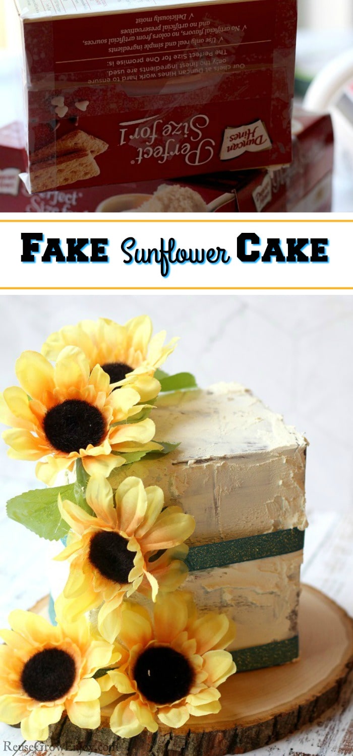 A finished fake cake prop with sunflowers and green ribbon. It is on a wood slice at bottom. Top is boxes used to make it. Text overlay that says "Fake Sunflower Cake".