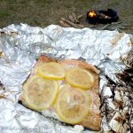 campfire cooked salmon on foil with lemon slices. Campfire in background.