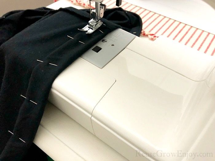Black dress on the sewing machine sticking the fold in place.