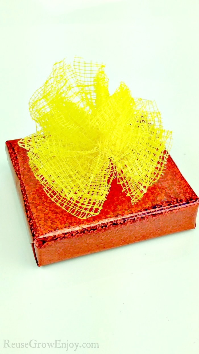 Red wrapped gift with yellow mesh produce bags made into bow on top.