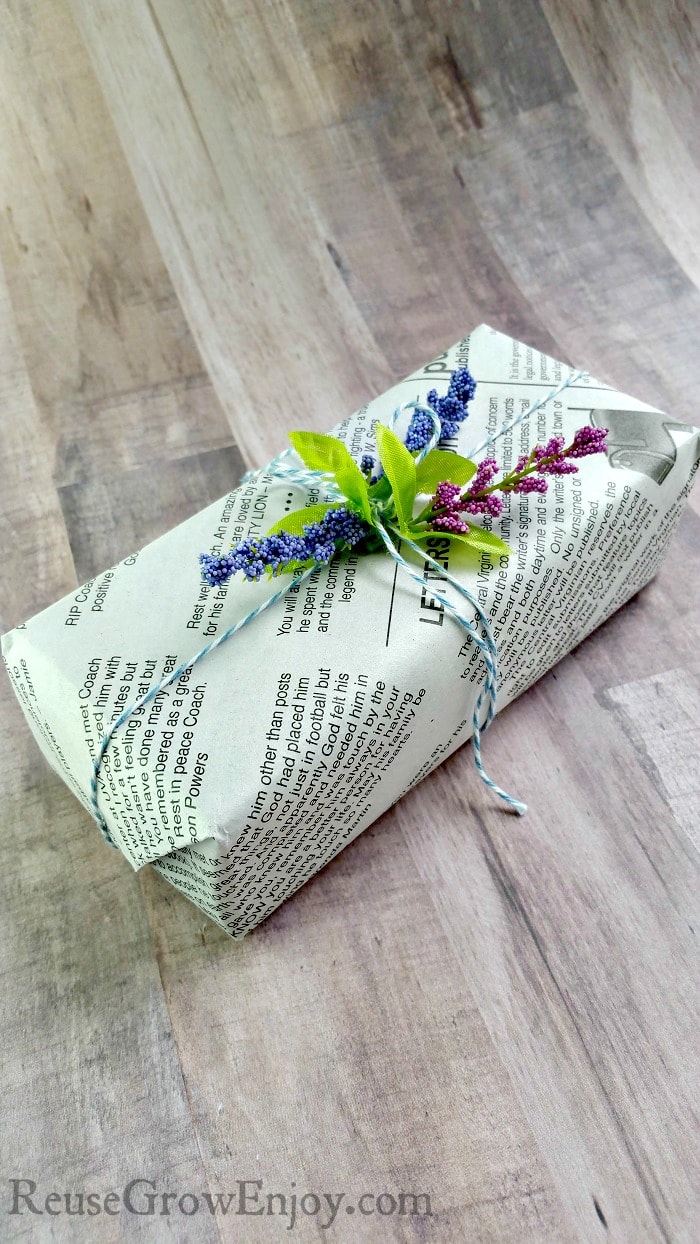 Small gift wrapped in newspaper with flowers on top.