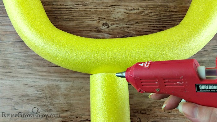 A red hot glue gun gluing a piced of pool noodle to the U shaped piece