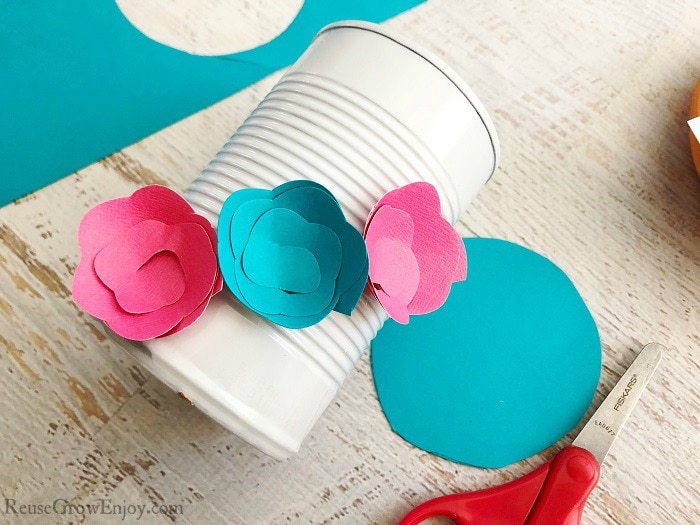 Pink and blue paper flowers being attached to white can.