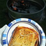 Grilled Cheese on plate with campfire in background.