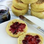 open english muffin on white plate with jelly, stack of english muffins and jelly jar in background