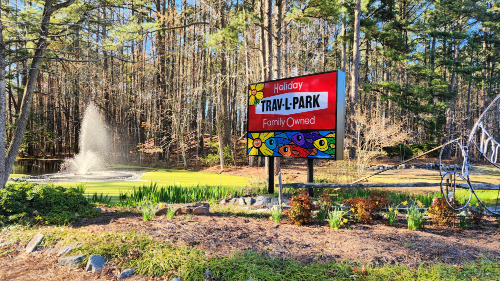 Holiday Trav-L-Park Sign by road with water fountain in pond