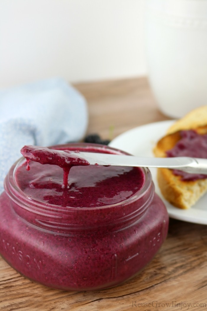 Small glass jar of blackberry jelly with butter knife laying on top