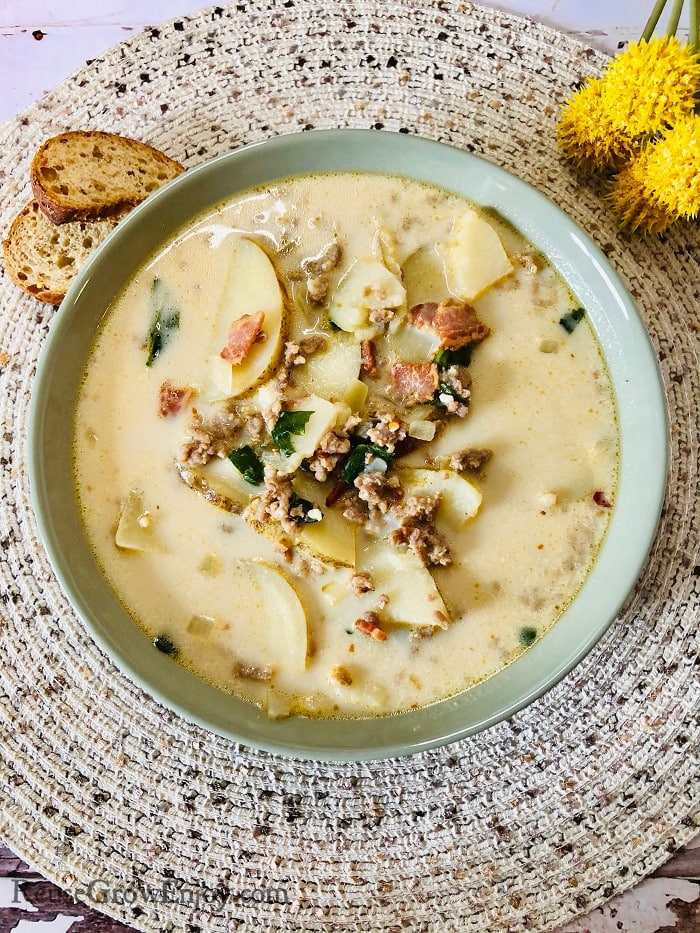 Bowl of zuppa toscana soup with bread slices to the left of the bowl