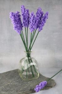 Glass bottle full of lavender felt flowers sitting on slate